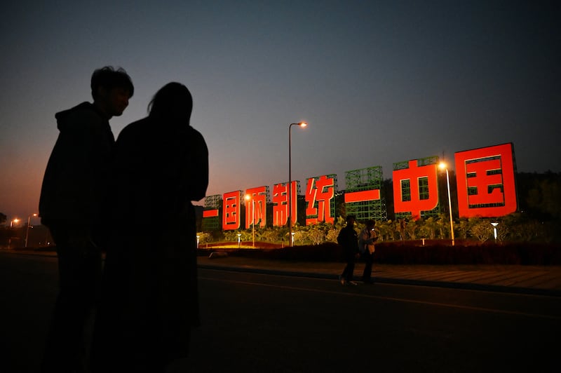 A couple stands near a giant propaganda slogan which reads “One Country, Two Systems, Unify China”, which can be seen from Taiwan’s Kinmen Island, on a sidewalk on the waterfront in Xiamen, in China’s southeast Fujian province on Jan. 10, 2024.